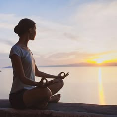 a woman sitting on the edge of a cliff doing yoga