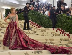 a woman in a red and gold gown standing on steps with cameras around her, taking pictures