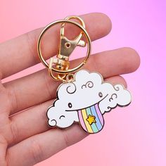 a hand holding a keychain with a cartoon cloud and rainbow on the front