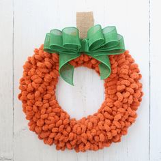 an orange and green wreath hanging on the side of a white door with a green bow