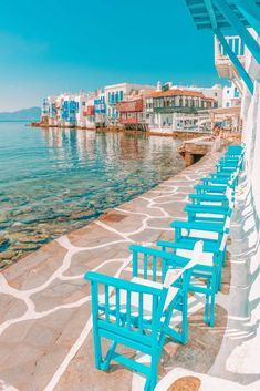 blue chairs are lined up along the water's edge in front of white buildings