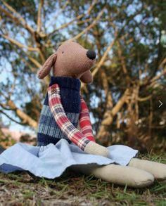 a teddy bear sitting on top of a blue blanket in front of some trees and grass