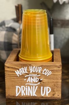 a wooden box with a yellow cup and drink up sign on it sitting on a table