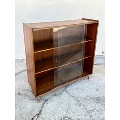 a wooden bookcase with glass doors on the front and bottom shelves, against a white brick wall