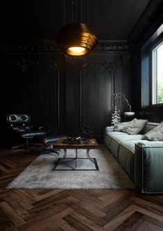 a living room with black walls and wood flooring is lit by a pendant light