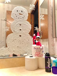 a snowman made out of toilet paper sitting in front of a bathroom mirror next to two rolls of toilet paper