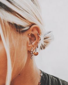 a woman with blonde hair wearing gold earrings and a black shirt is looking down at her ear