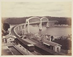 an old black and white photo of a train going over a bridge on the water