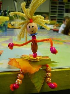 a toy doll is sitting on top of a table in front of some children's artwork