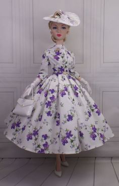 a doll wearing a white dress with purple flowers on it's skirt and hat