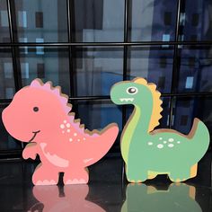 two wooden dinosaurs standing next to each other on a table in front of a window