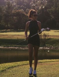 a woman holding a golf club on top of a grass covered field next to a lake