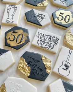 decorated cookies with gold and black frosting are arranged on a white tablecloth that says 50th