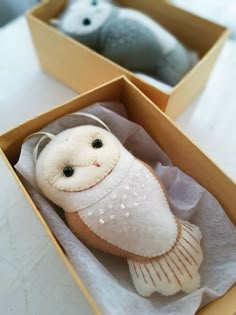 two stuffed animals in boxes on a white tableclothed surface, one is an owl and the other is a fish