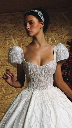 a woman in a white wedding dress with a tiara on her head standing next to hay