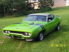 a green muscle car parked on top of a lush green grass covered field in front of a barn