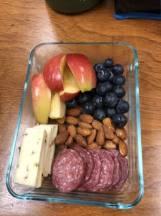 a glass container filled with fruit, nuts and meats on top of a wooden table