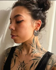 a woman with tattoos on her chest and shoulder is looking down at the camera while wearing large earrings