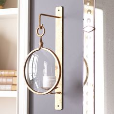 a wall mounted magnifying glass hanging from a hook on a gray wall with bookshelves in the background