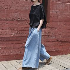 a woman in black shirt and blue jeans walking on wooden floor next to brick wall