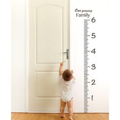 a baby standing in front of a growth chart wall decal