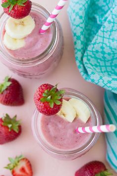 two glasses filled with smoothie and strawberries next to each other on a pink surface