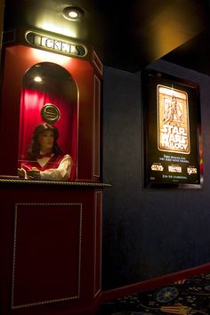 a woman is sitting in a red machine at the entrance to a movie theater with posters on the wall behind her