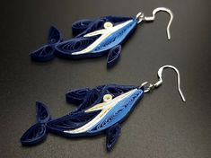 two blue fish shaped earrings with white and yellow accents on black surface, side by side