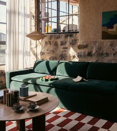 a green couch sitting in front of a window next to a table with food on it