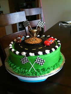 a birthday cake decorated with racing cars and flags on top of a wooden dining room table