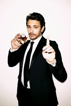 a man in a suit and tie holding a bottle of whiskey with his finger up