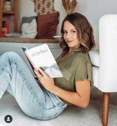 a woman is sitting on the floor reading a book and smiling at the camera with her legs crossed