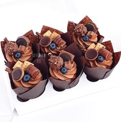 four cupcakes with chocolate frosting and blueberries on top in a box