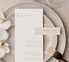 a table setting with white flowers and place cards on it, along with a gold fork