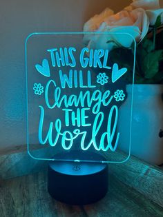 this girl will change the world neon sign on a table next to a vase with flowers