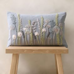 a blue pillow with white flowers on it sitting on a wooden stool next to a wall