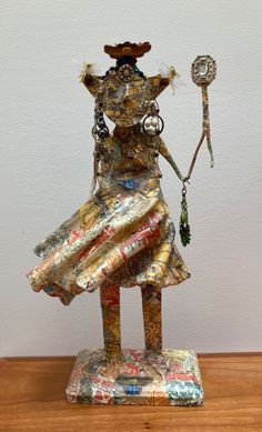 a statue made out of old magazines on a wooden table next to a white wall