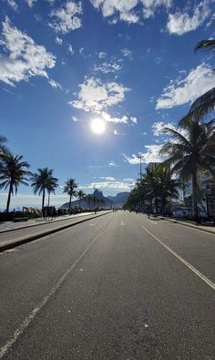 an empty street with palm trees on both sides and the sun in the sky above