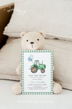 a teddy bear sitting on top of a bed holding a card with an image of a tractor