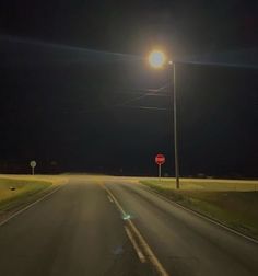 an empty road at night with street lights and stop sign in the foreground on one side