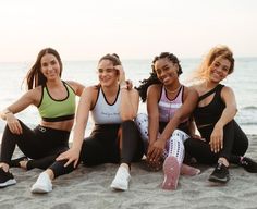 four women are sitting on the beach and smiling