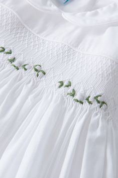 an embroidered white dress with green leaves on it