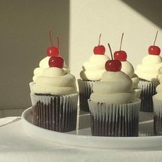 several cupcakes with white frosting and cherries on top sit on a plate