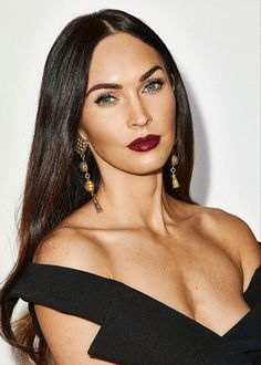 a woman with long dark hair wearing gold earrings and a black off the shoulder dress