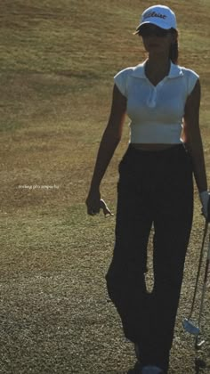 a woman walking across a grass covered field with a golf club in her left hand