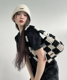 a woman with long hair wearing a black and white crochet bag while standing in front of a white wall