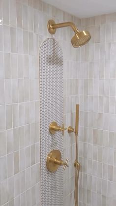 a shower head with gold faucet and handset in a white tiled bathroom