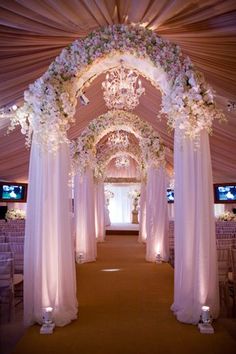 the inside of a wedding venue decorated with white flowers and chandelier draped over it