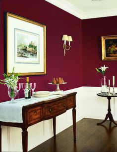 a dining room with red walls and white trim on the walls is decorated with art