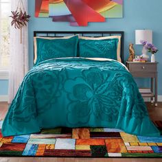 a bedroom with blue walls and a bed covered in a turquoise comforter, pillows and blankets